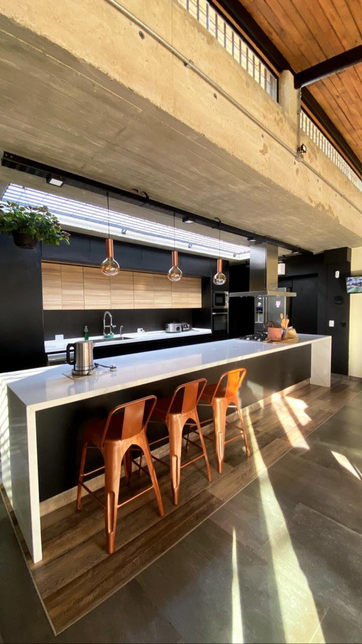 Cocina a medida con isla central, banquetas de metal color cobre y alacenas de madera